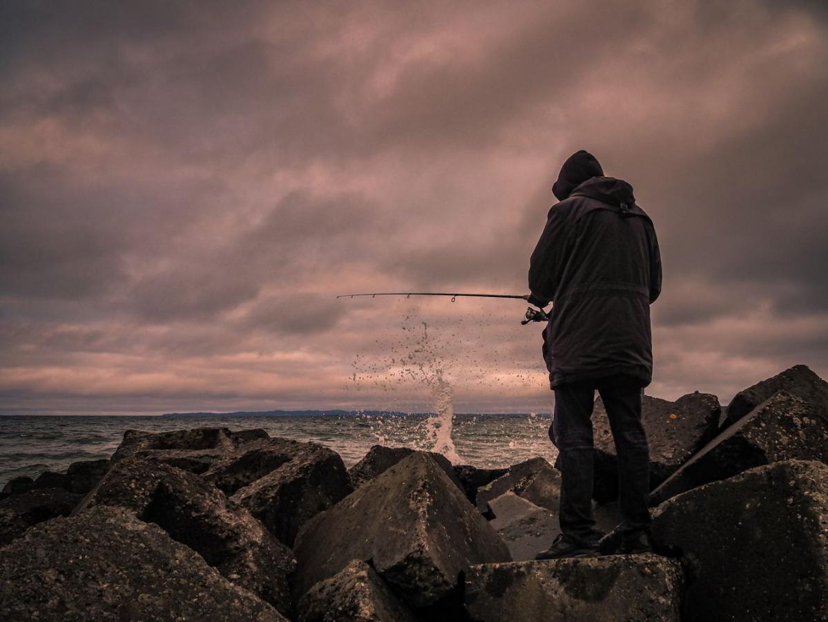 Mand står med ryggen til i blæsevejr og fisker i havet