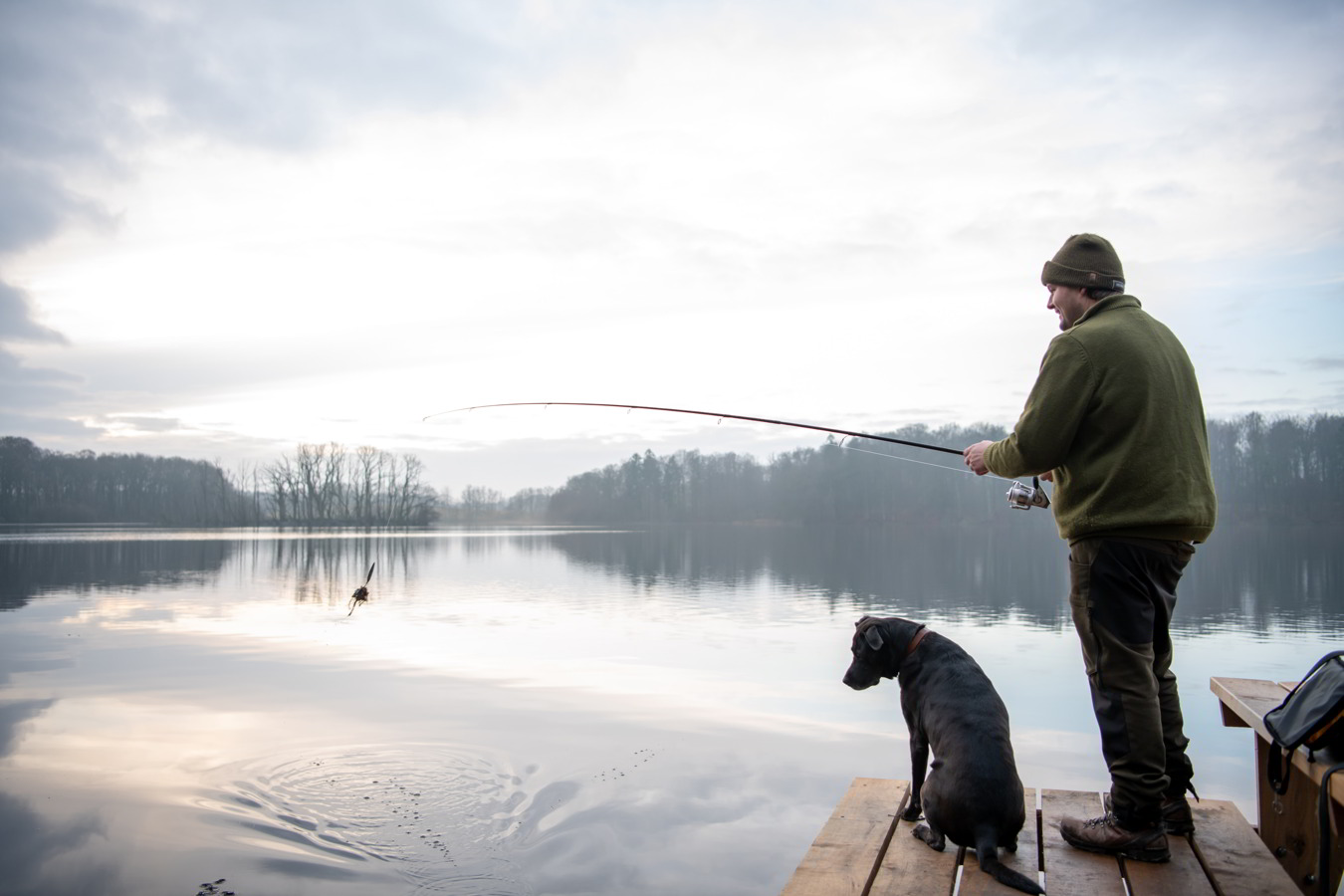 Mand og hund fisker ved en sø og kigger efter tang på en fiskekrog