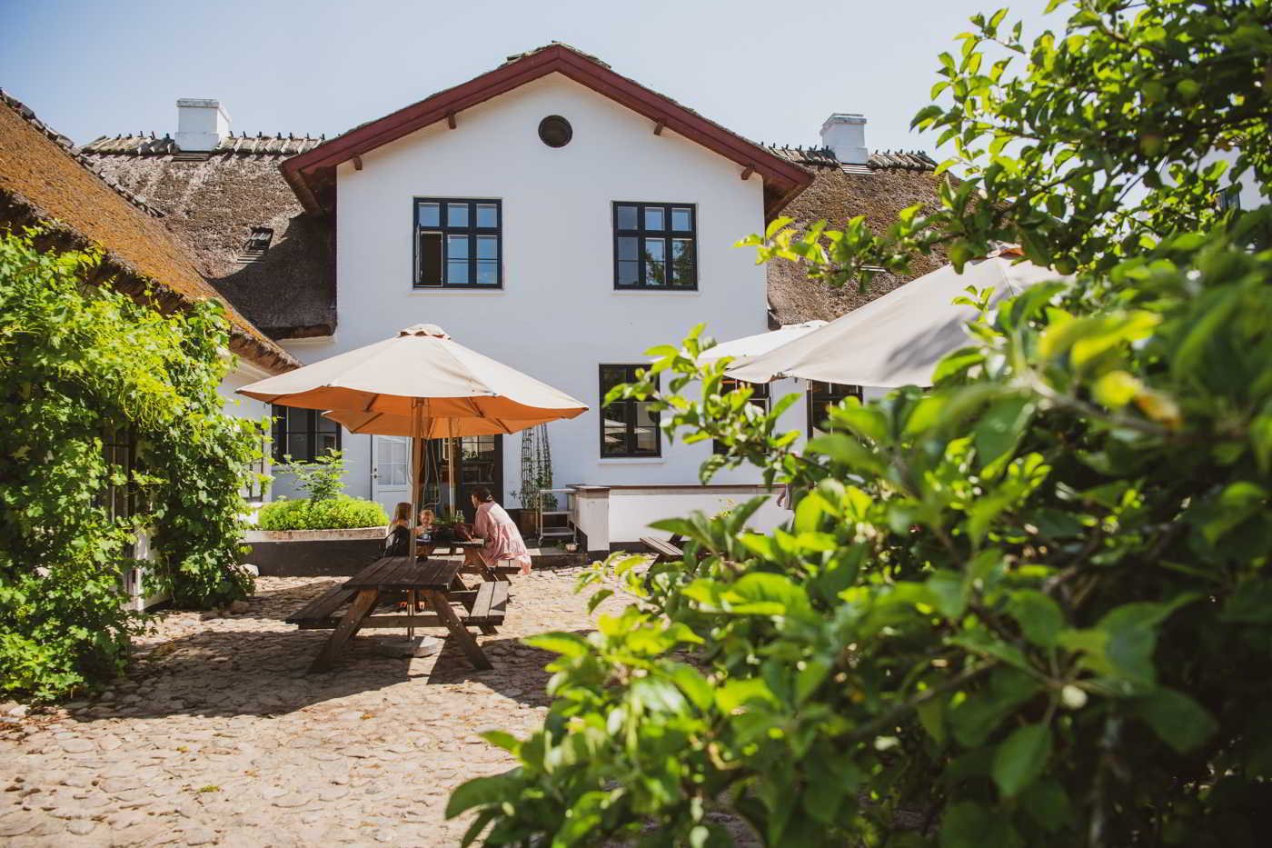 Eine Mutter und ihre Kinder essen unter einem Sonnenschirm im Innenhof des Møllecafé am Esrum Kloster.