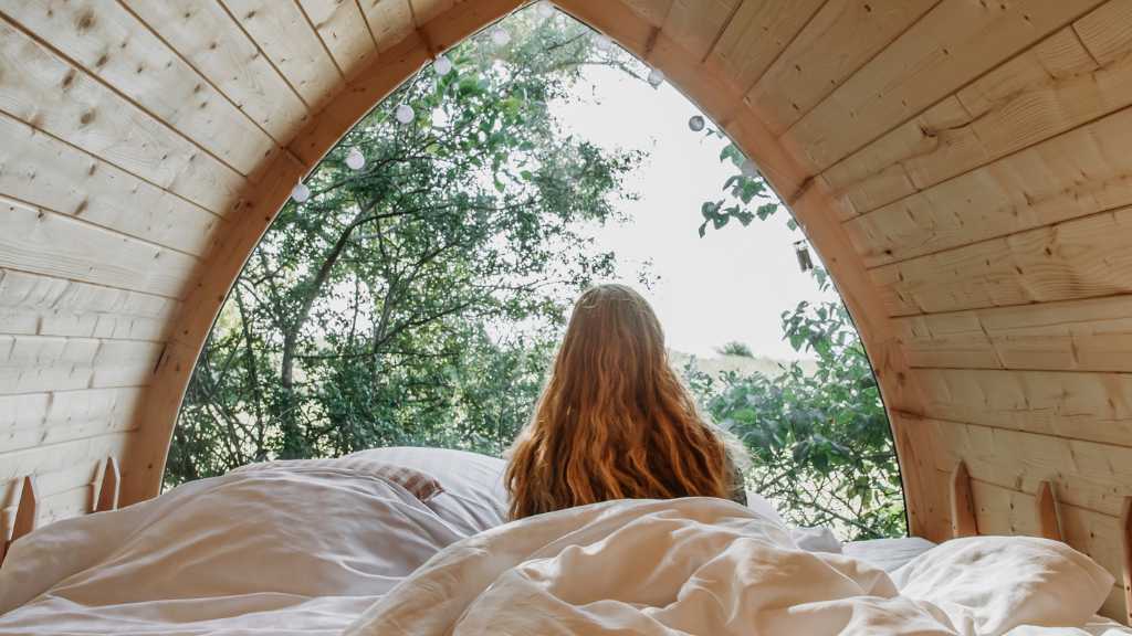  A woman sits wrapped in blankets, gazing out into nature in a surf shack at Lynæs Surfcenter.