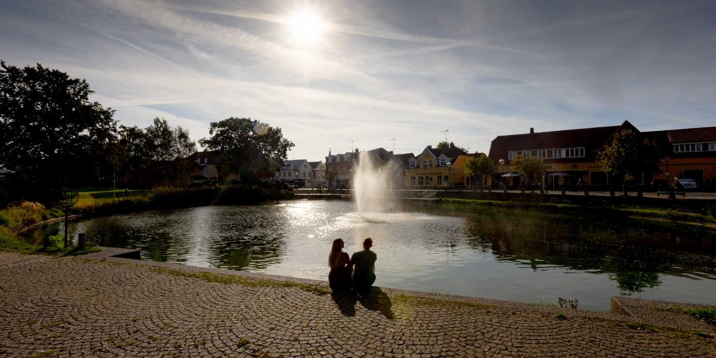Et par sidder og kigger ud over Helsinge gadekær i aftensolen