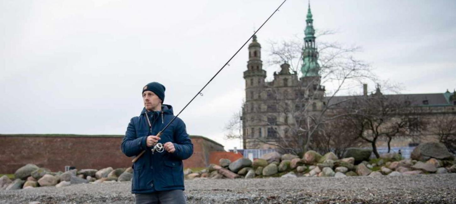 Mand fisker i havet ved Øresund med Kronborg i baggrunden