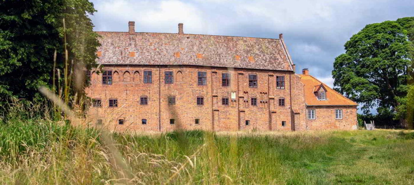 Esrum Monastery's red brick building is located at the end of a large grassy field.