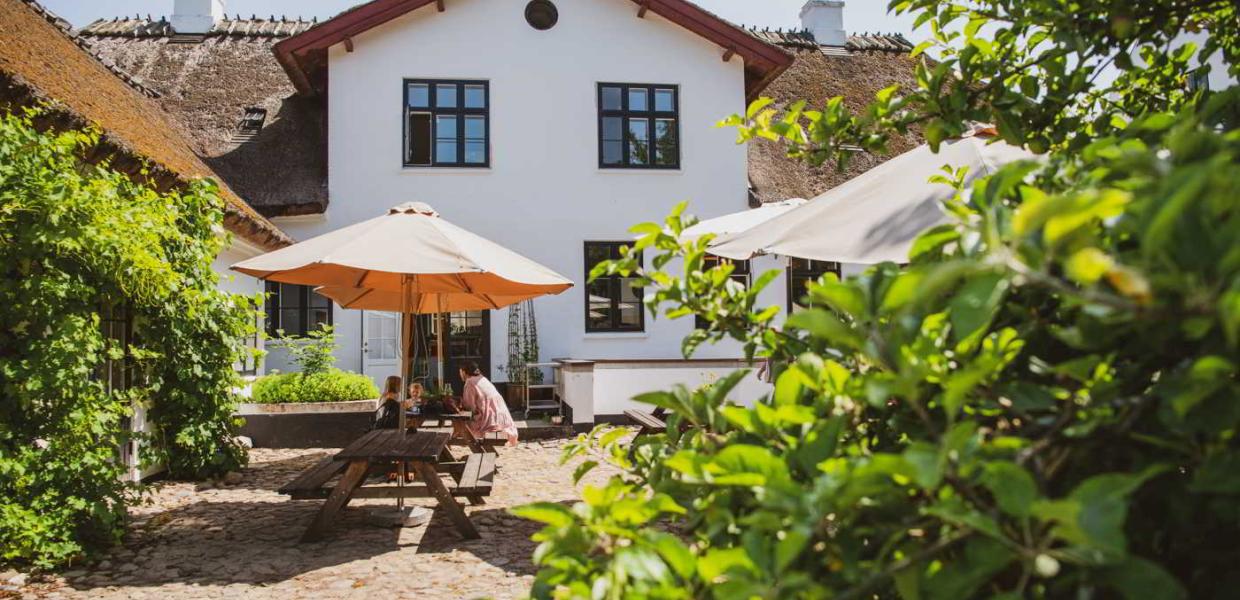 A mother and her children are eating under an umbrella in the courtyard garden at the Mill Café near Esrum Kloster.