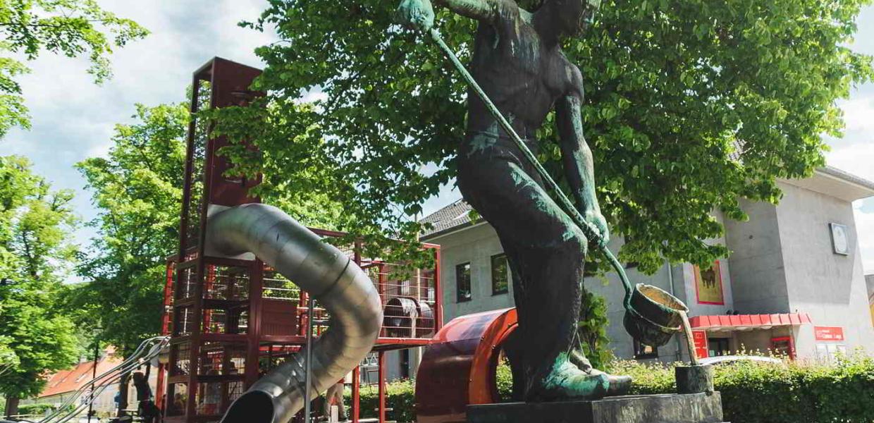 The playground in Frederiksværk with the large slide in the background and a statue of a worker in the foreground.