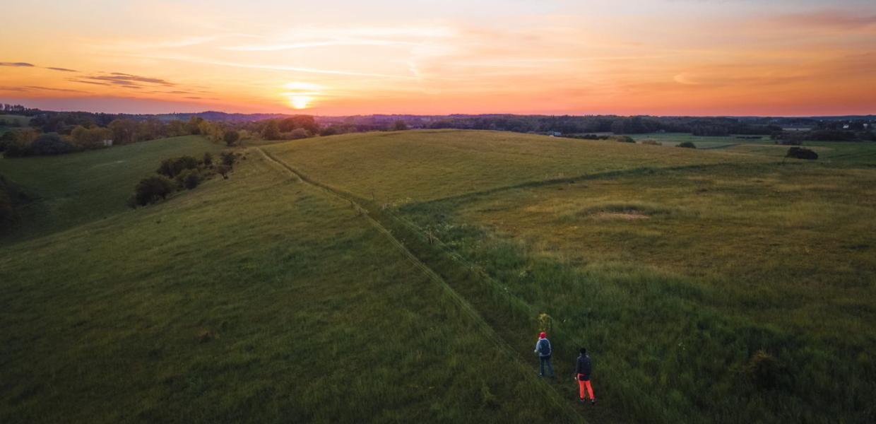 A drone films two hikers on a meadow at Halsninoen in North Zealand