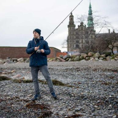 Mand fisker i havet ved Øresund med Kronborg i baggrunden