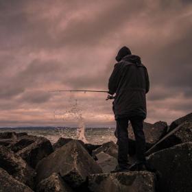 Mand står med ryggen til i blæsevejr og fisker i havet